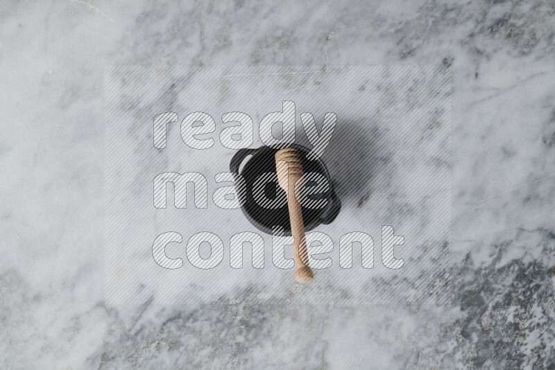 Black pottery bowl with wooden honey dipper in it on grey marble background
