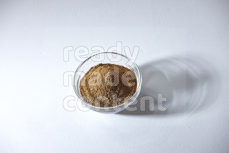 A glass bowl full of cumin powder on a white flooring