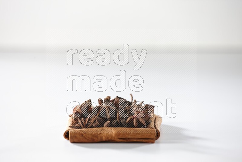 أربعة من أعواد القرفة مكونة شكل مربع بداخلها يانسون نجمي علي خلفية بيضاء