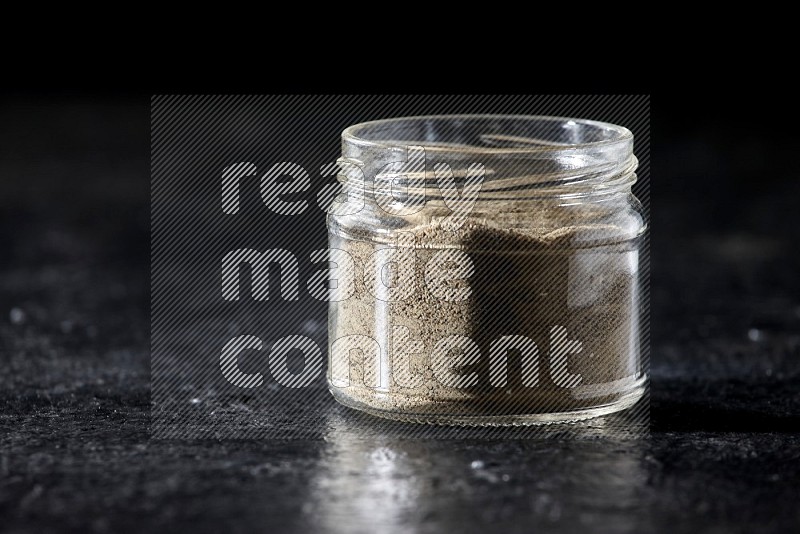 A glass jar full of white pepper powder on textured black flooring
