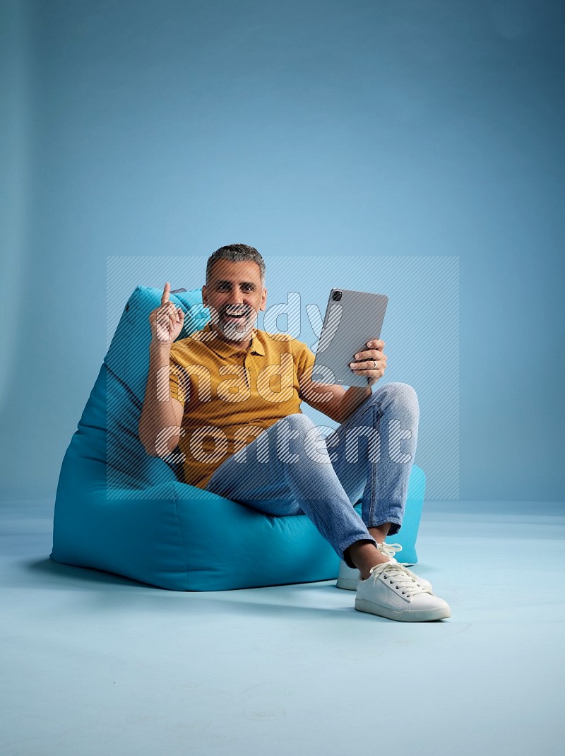 A man sitting on a blue beanbag and working on tablet