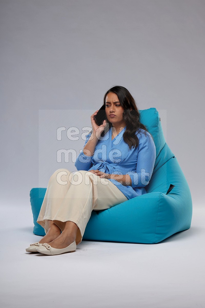 A woman sitting on a blue beanbag and talking on the phone