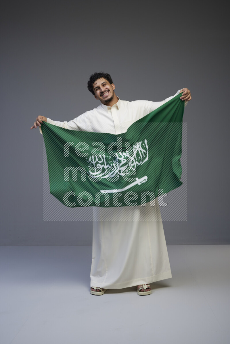 رجل سعودي يرتدي ثوب ويحمل علم السعودية