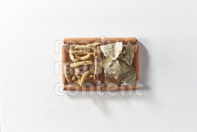 مربعان من أعواد القرفة ممتلئان بأصابع الكركم وأوراق الغار علي خلفية بيضاء