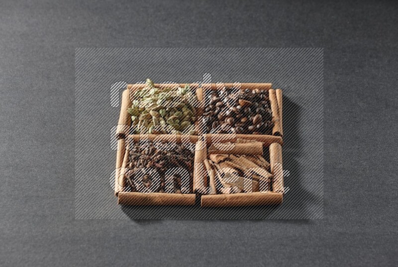 4 مربعات من عيدان القرفة ممتلئة بحبوب القهوة وقطع القرفة والقرنفل وحبوب الهيل على أرضية سوداء