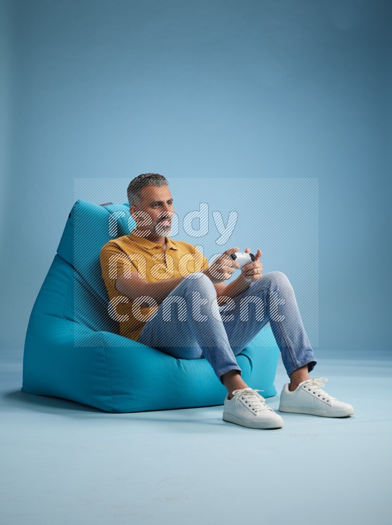 A man sitting on a blue beanbag and gaming with joystick