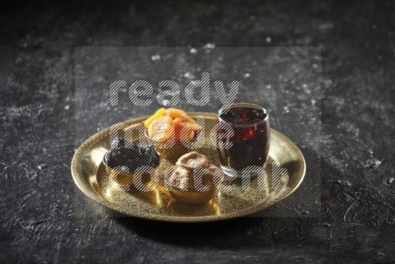 Dried fruits in metal bowls with tamarind on a tray in dark setup