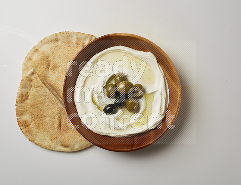 Lebnah garnished with whole olives in a wooden plate on a white background