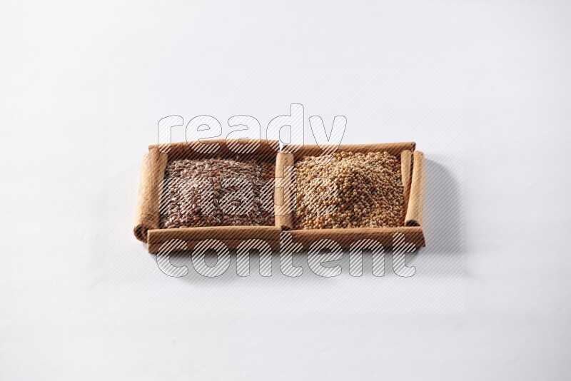 مربعان من أعواد القرفة ممتلئان بحبوب الخردل وبذور الكتان علي خلفية بيضاء