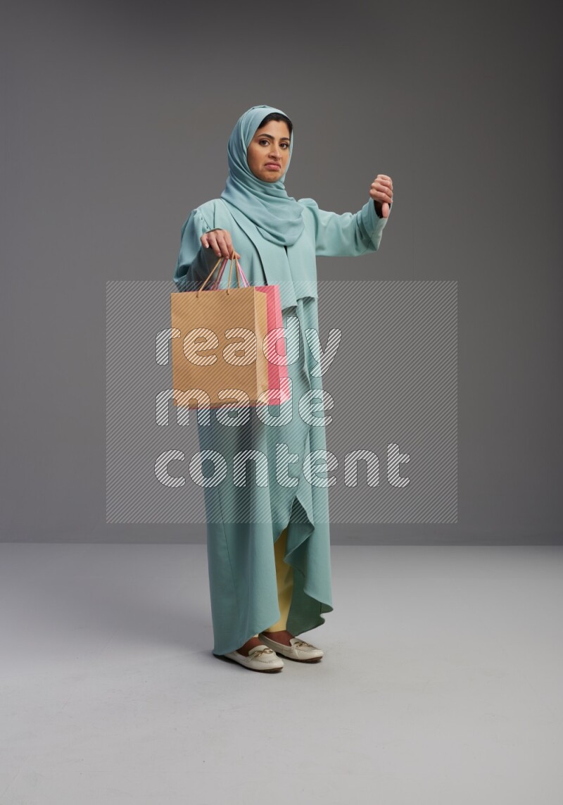 Saudi Woman wearing Abaya standing holding shopping bag on Gray background