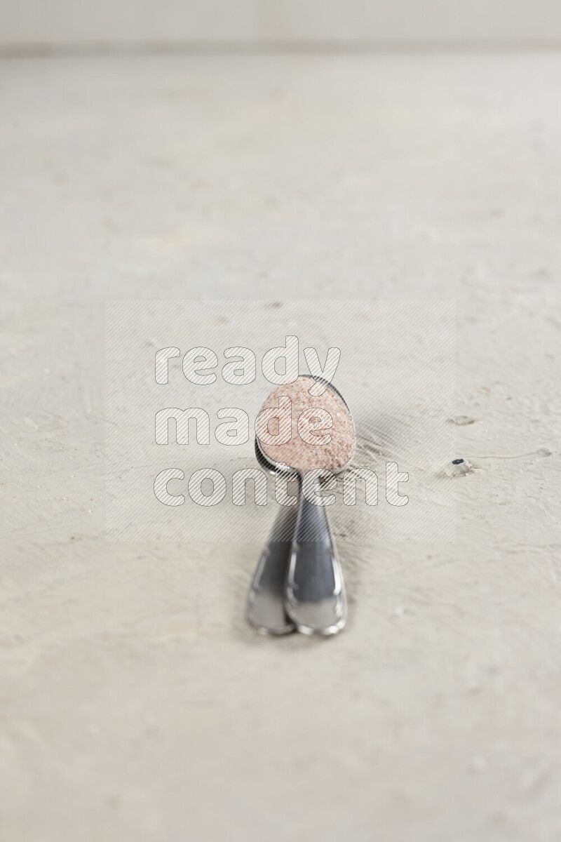 2 metal spoons filled with fine table salt and fine pink himalayan salt on white background
