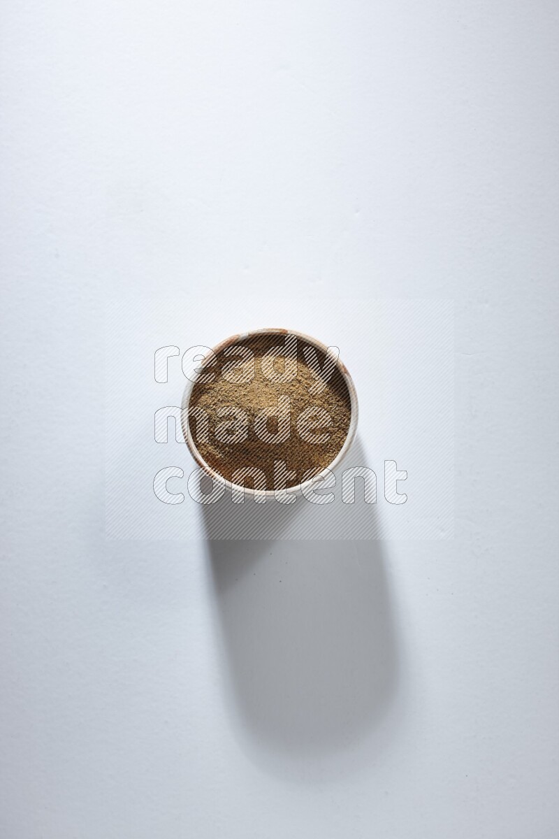 A beige bowl full of cumin powder on a white flooring
