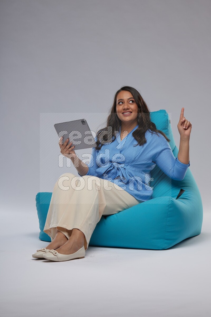 A woman sitting on a blue beanbag and working on tablet