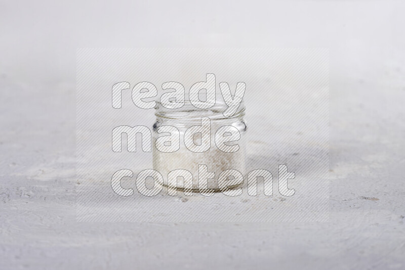 A glass jar full of coarse sea salt crystals on white background