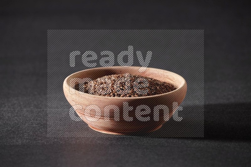 A wooden bowl full of flaxseeds on a black flooring
