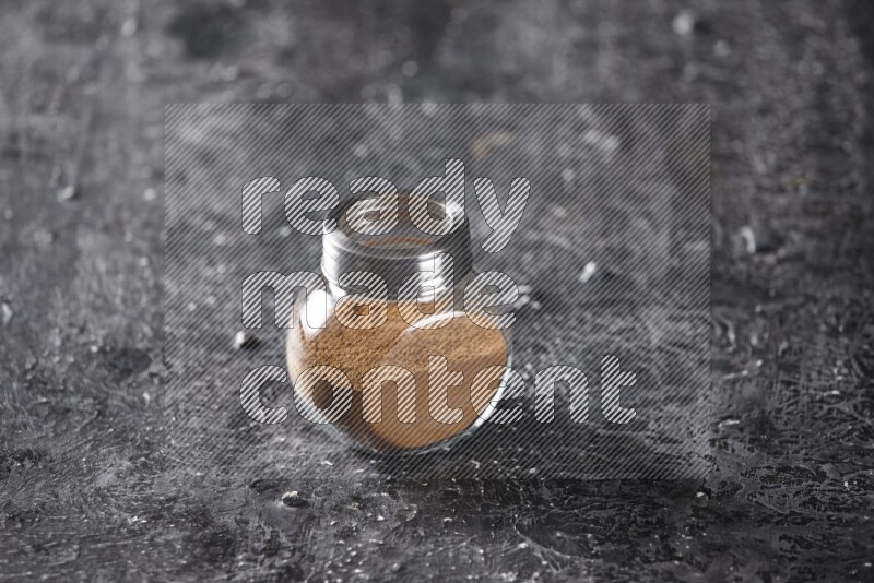 Herbal glass jar full of cinnamon powder on a textured black background