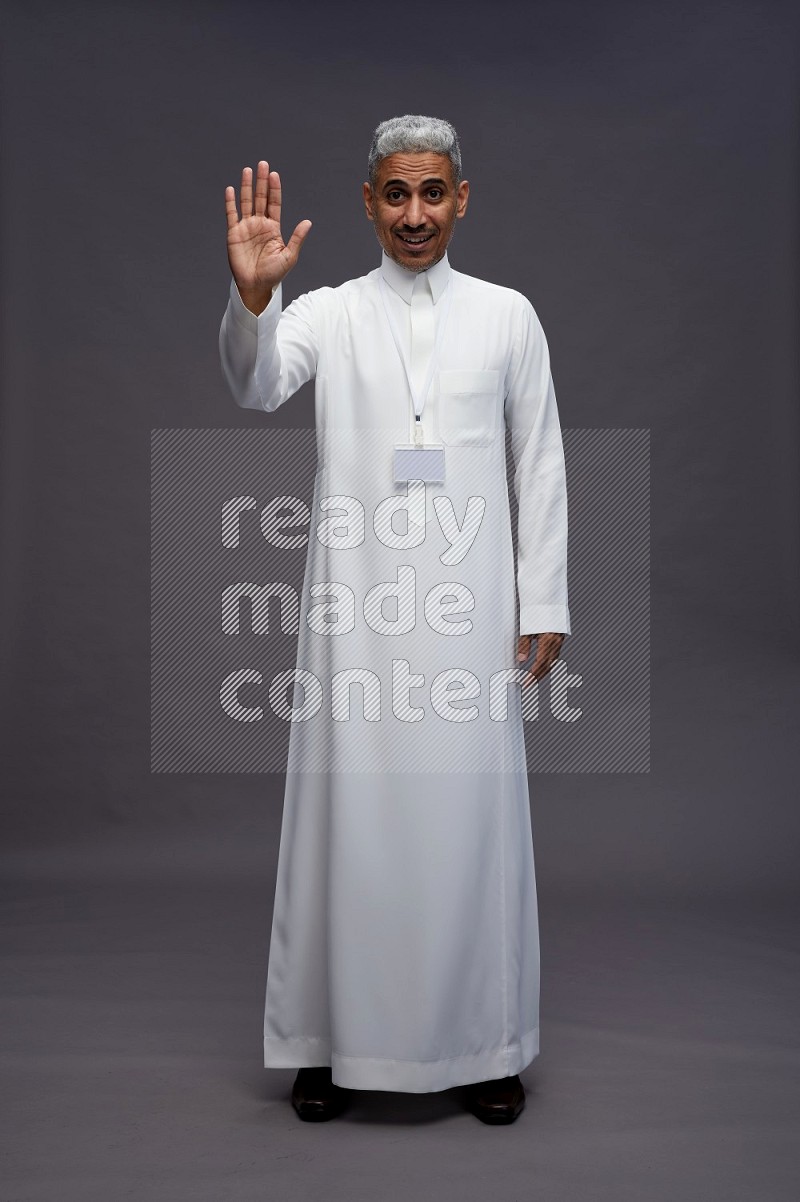 Saudi man wearing thob with neck strap employee badge standing interacting with the camera on gray background