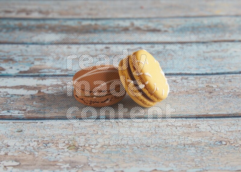 45º Shot of of two assorted Brown Irish Cream, and Yellow Piña Colada macarons on light blue background