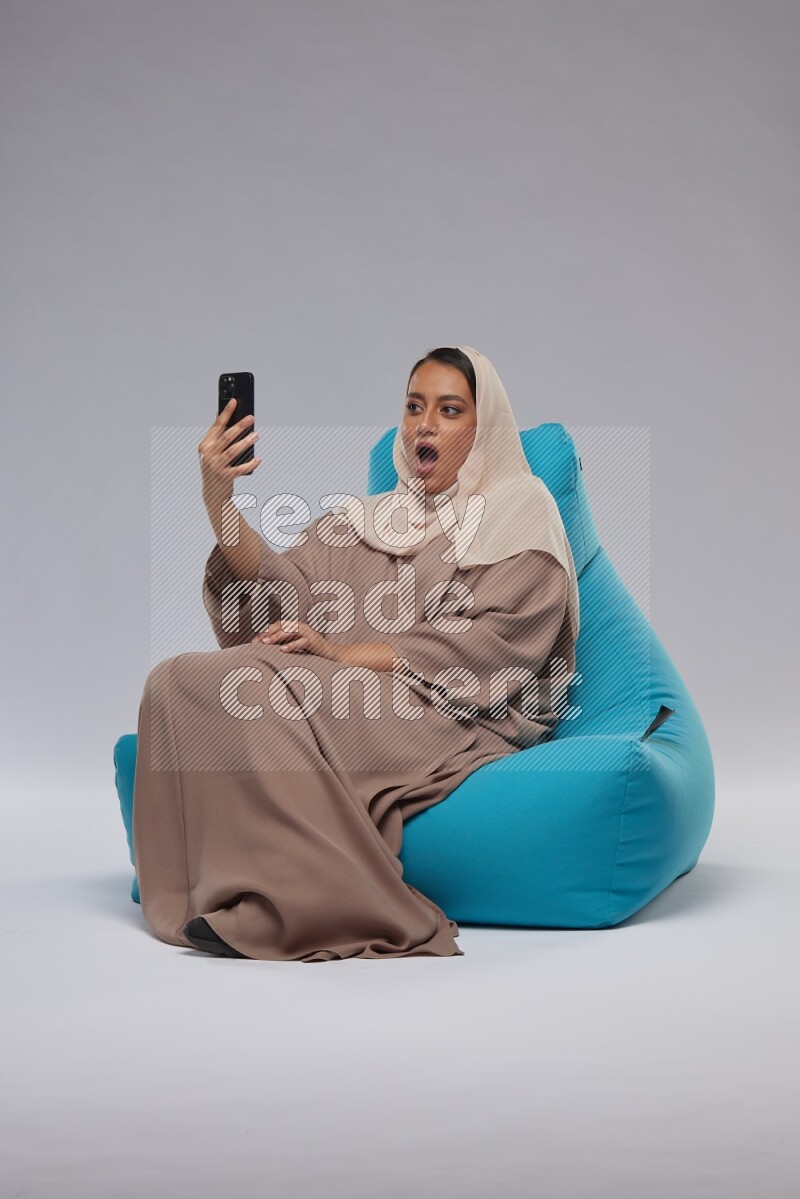 A Saudi woman sitting on a blue beanbag and taking selfie