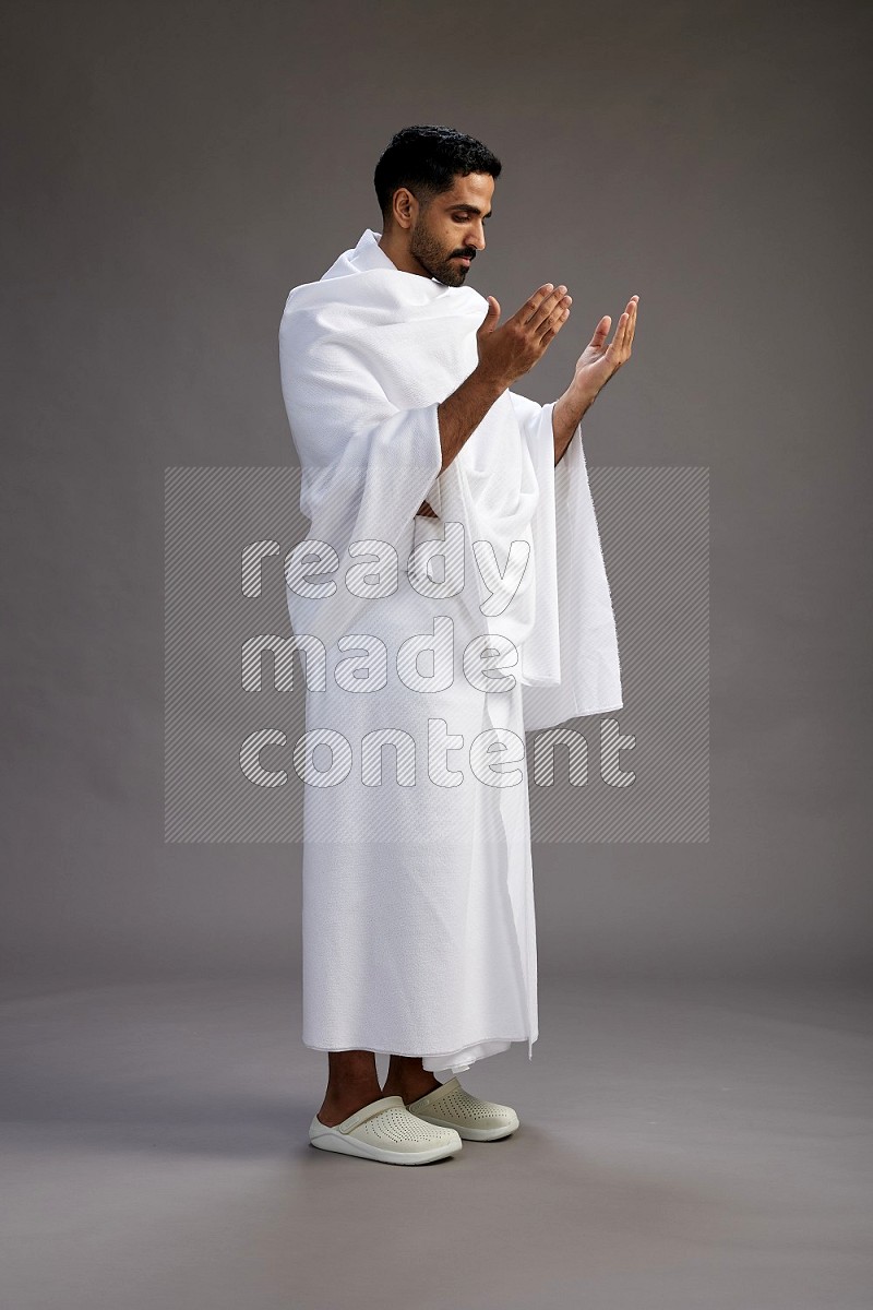 A man wearing Ehram Standing performing dua'a on gray background
