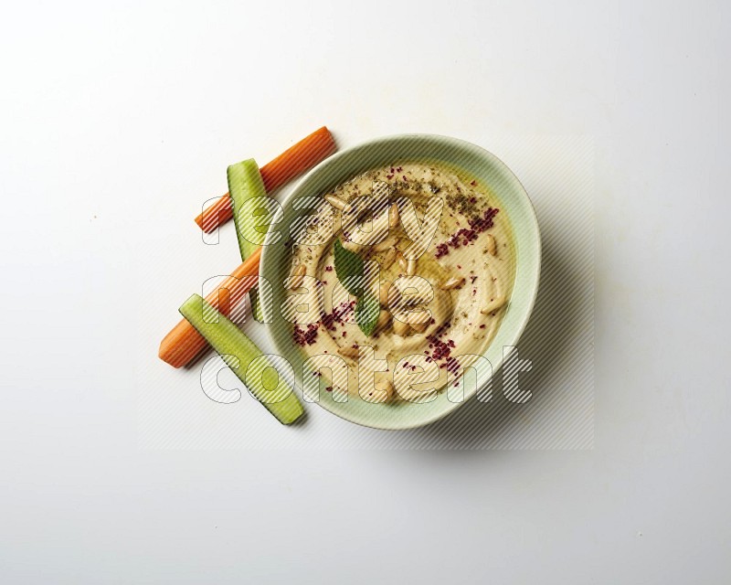 Hummus in a green plate garnished with zattar & sumak on a white background