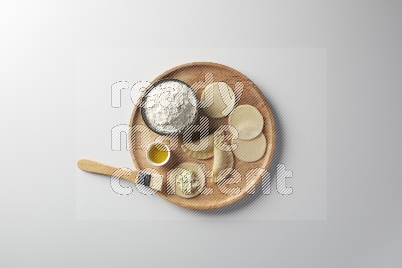 two closed sambosas and one open sambosa filled with cheese while flour, and oil with oil brush aside in a wooden dish on a white background
