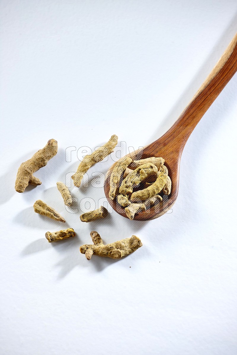 A wooden ladle full of dried turmeric fingers on white flooring