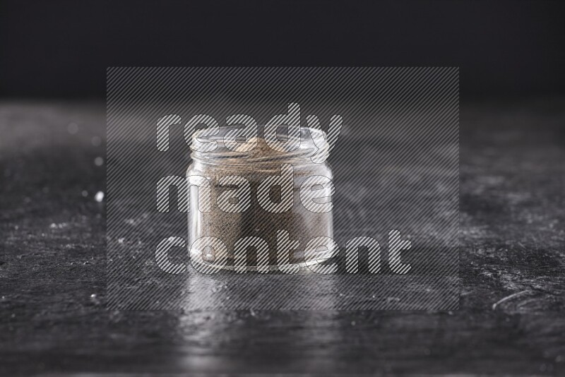 بودرة الفلفل الأسود في وعاء زجاجي علي خلفية سوداء