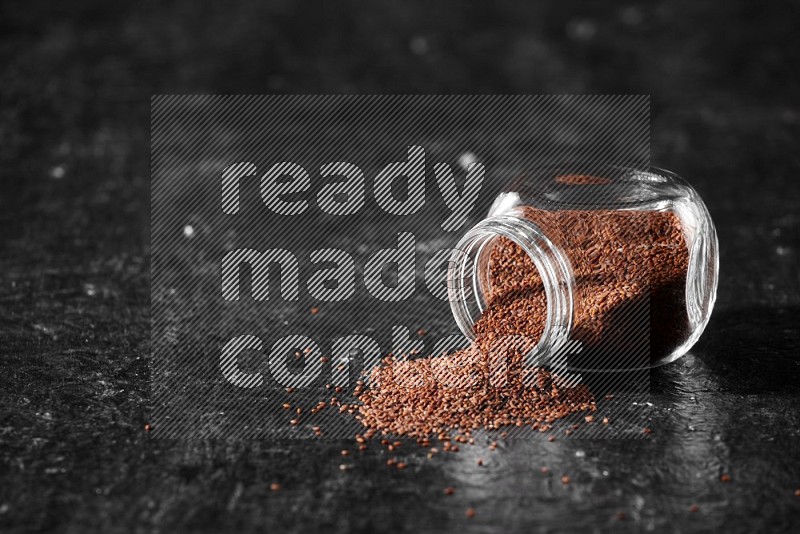 A glass spice jar full of garden cress seeds flipped and seeds spread out a textured black flooring