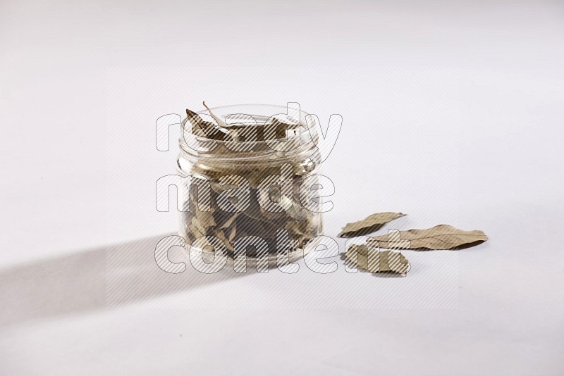 A glass jar filled with dried bay leaves on white flooring