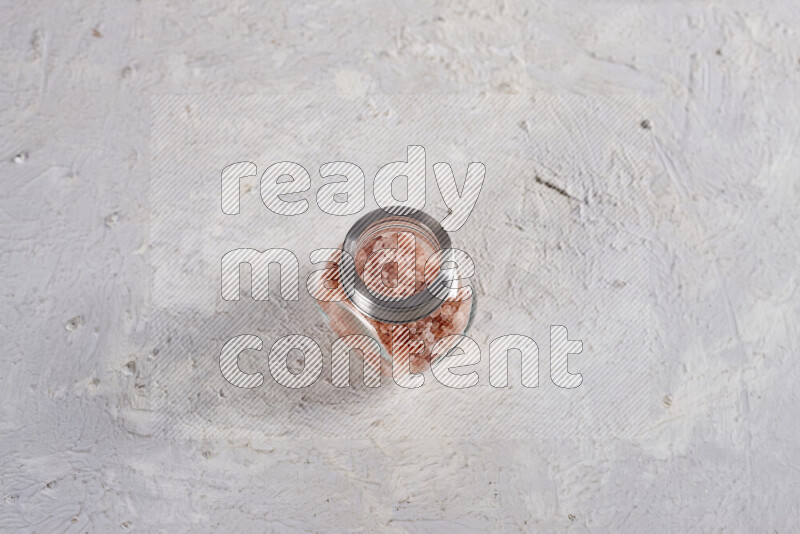 A glass jar full of coarse himalayan salt crystals on white background