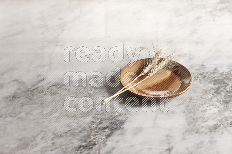 Wheat stalks on multicolored pottery plate on grey marble background