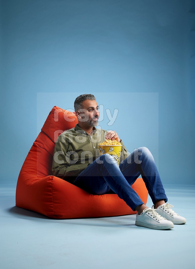 A man sitting on an orange beanbag and eating popcorn