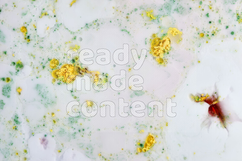 The image captures a splatter of yellow, red and green paint over a white backdrop
