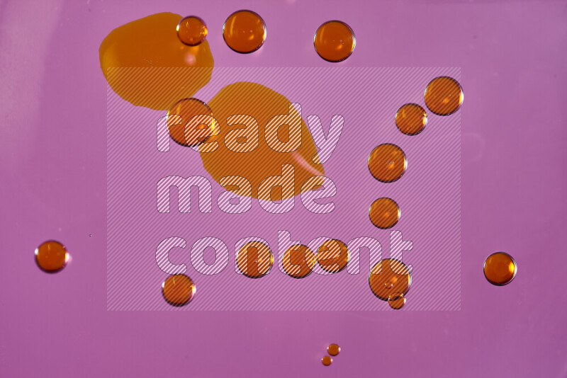 Close-ups of abstract orange watercolor drops on oil Surface on pink background