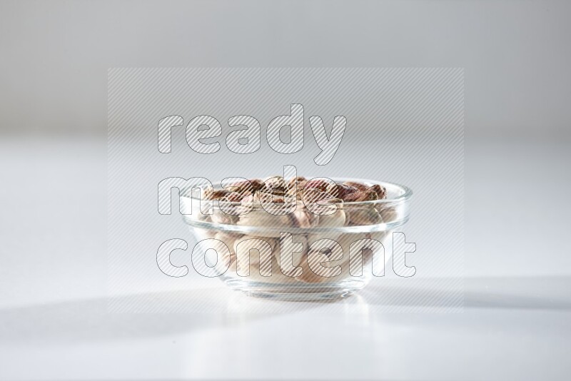 A glass bowl full of peeled pistachios on a white background in different angles