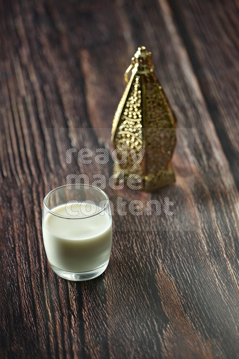 A golden lantern with different drinks, dates, nuts, prayer beads and quran on brown wooden background