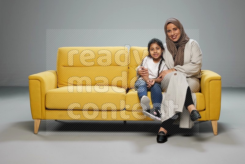A girl with her mother sitting and interacting with the camera on gray background