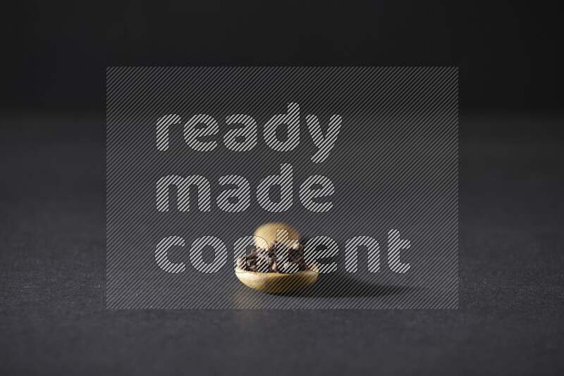 A wooden spoon full of cloves on a black flooring