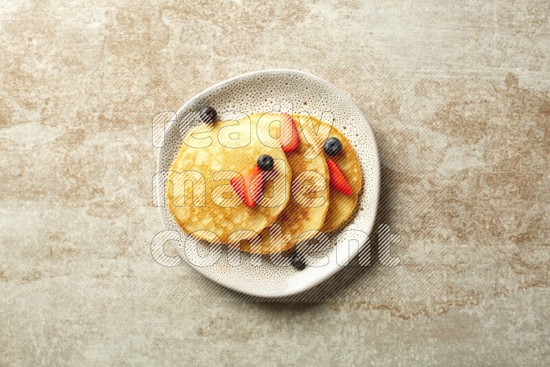 Three stacked mixed berries pancakes in an irregular plate on beige background