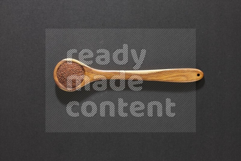 A wooden ladle full of garden cress seeds on a black flooring