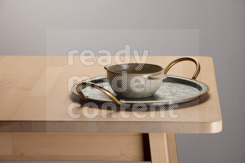 off white bowl placed on a rounded stainless steel tray with golden handels on the edge of wooden table