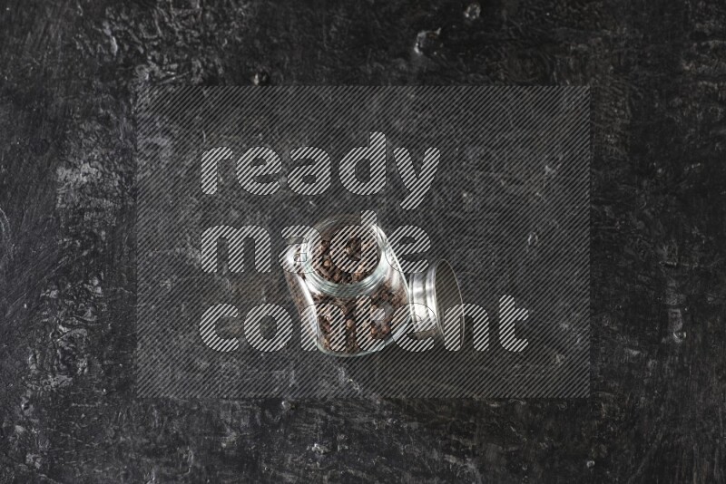 وعاء بهارات زجاجي ممتلئ بحبوب القرنفل على أرضية سوداء