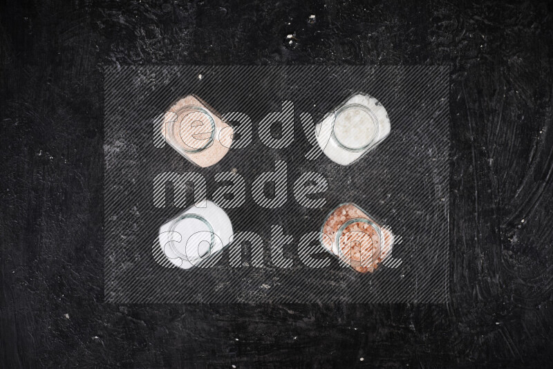 4 glass jars filled with table salt, coarse sea salt, fine himalayan salt and coarse himalayan salt on black background