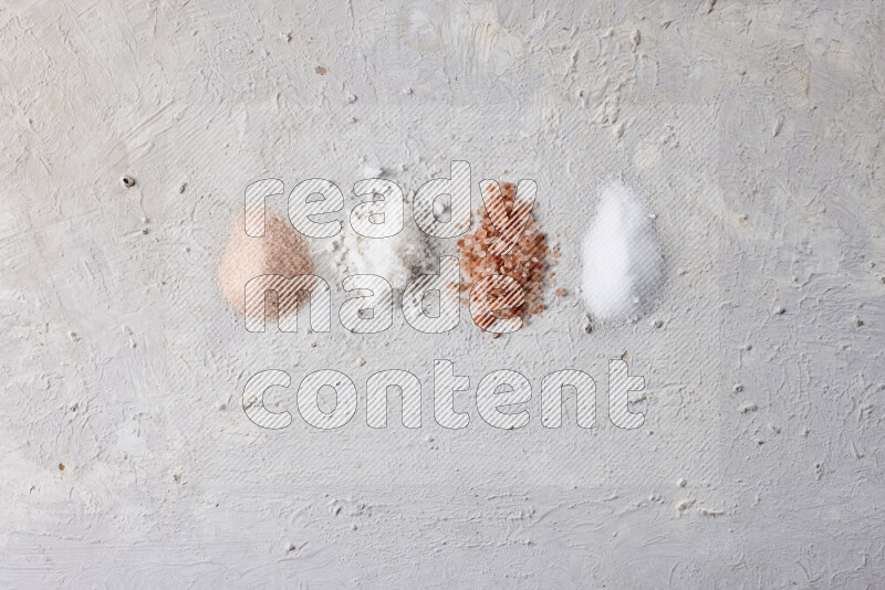 4 glass jars filled with table salt, coarse sea salt, fine himalayan salt and coarse himalayan salt on white background