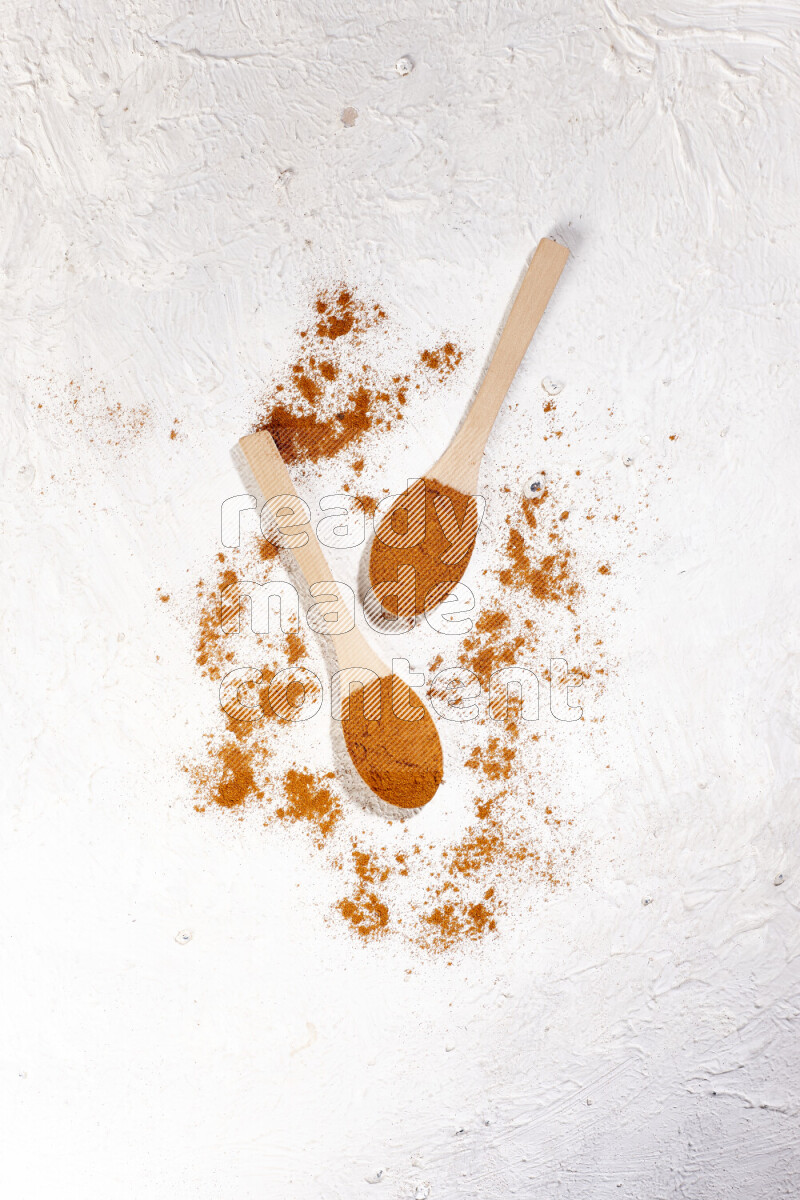 Two wooden spoons full of ground paprika powder on white background