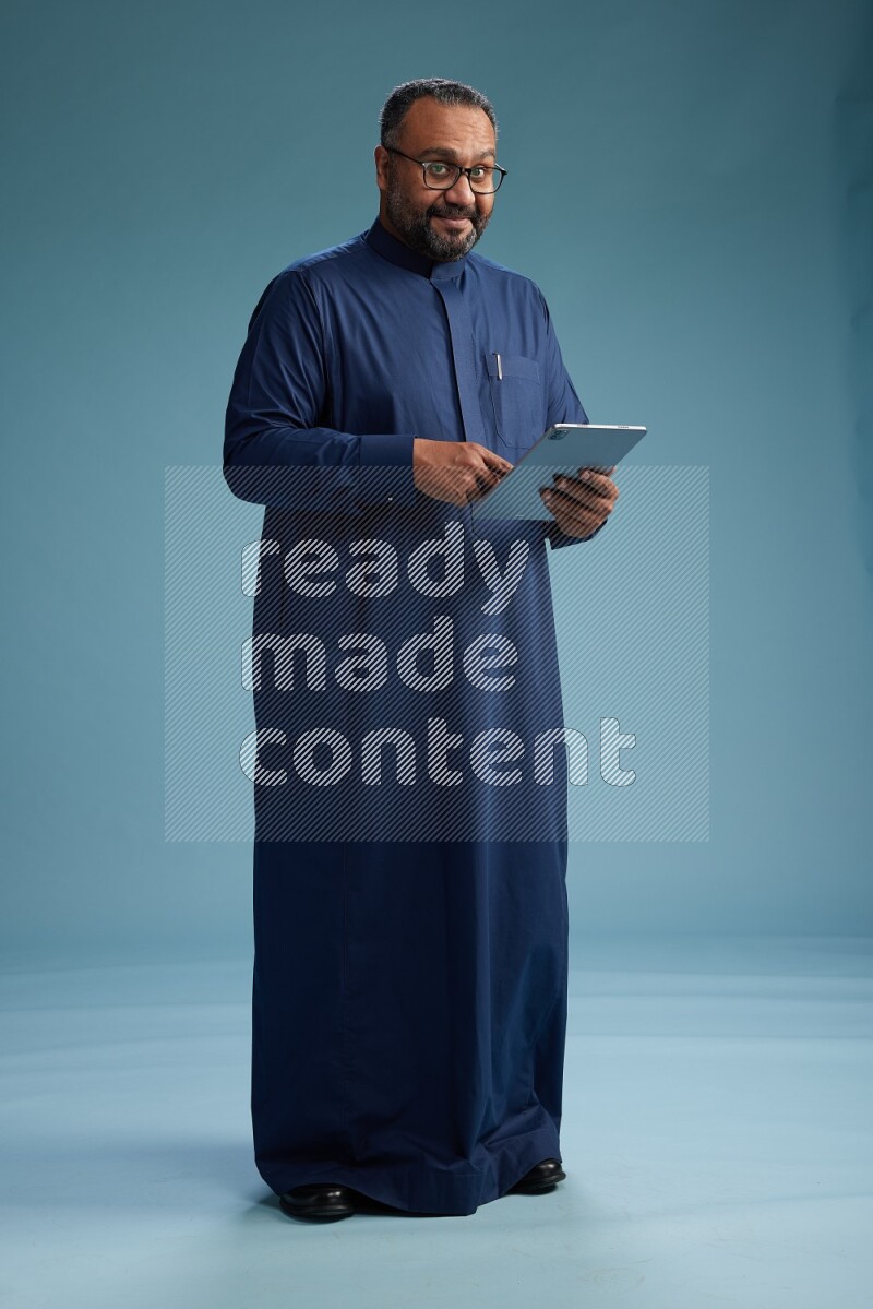 Saudi Man without shimag Standing working on tablet on blue background