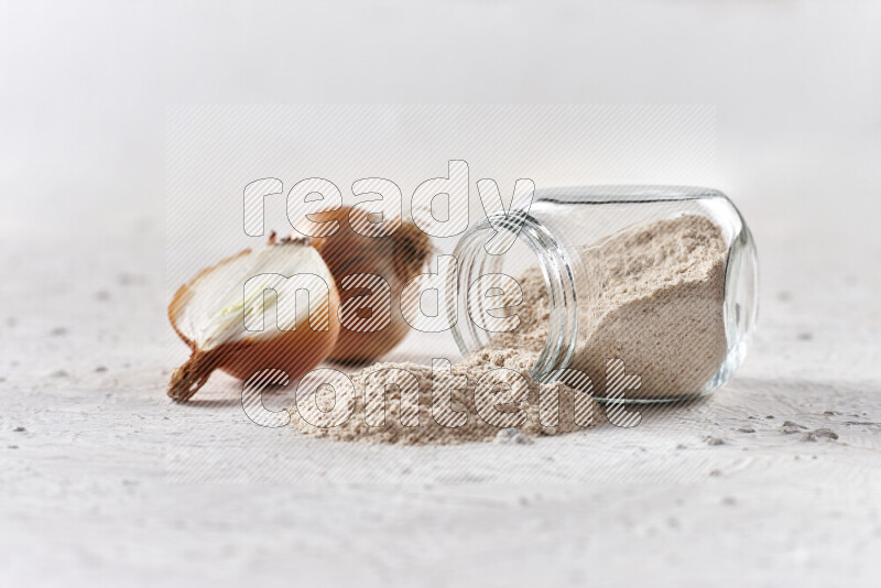 A glass jar full of onion powder flipped with some spilling powder on white background