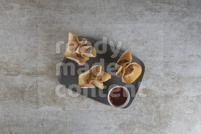 wonton cups with soy sauce ramkin on rectangle dark grey ceramic plate on grey textured counter top