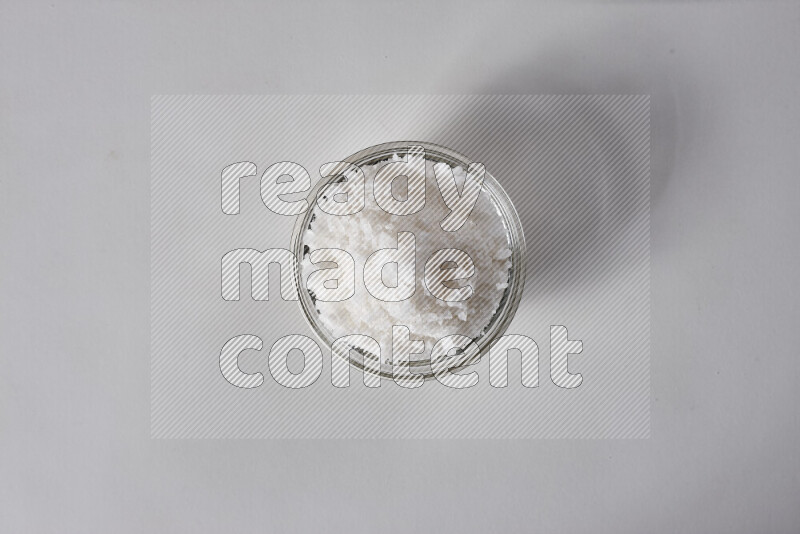 A glass bowl full of coarse sea salt crystals on white background